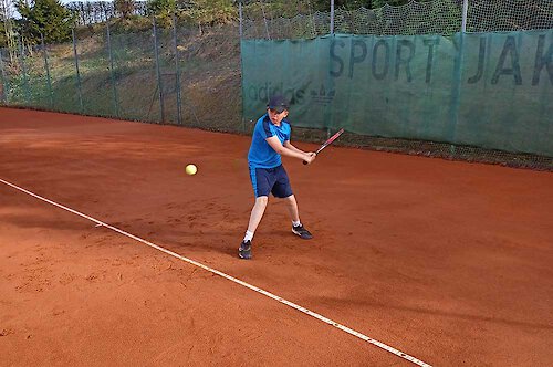 Ein Kind in blauer Sportkleidung schlägt nach einem Tennisball Tennistraining für Kinder im Bayerischen Wald.